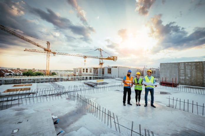 Construction industry and engineering in post-recession period Construction workers inspect building progress on site with cranes in the background
