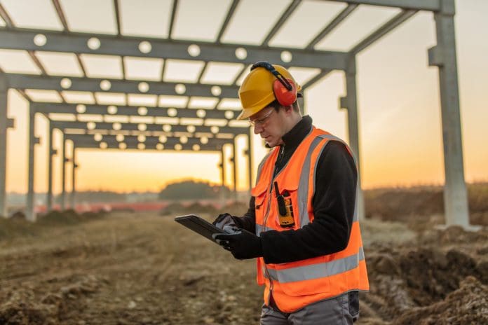 Architect using digital tablet at construction site A construction field worker in PPE analyzing data on a tablet