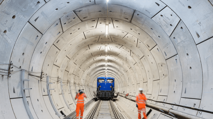 AtkinsRealis Image Rail Interior of a large rail tunnel with two workers in hi-vis clothing. Image: AtkinsRealis