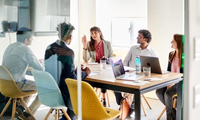 RLB data and ai academy A group of professionals sit around a table in an open plan office discussing training. construction consultancy Rider Levett Bucknall has launched a Data & AI Transformation Academy designed to digitally upskill its European teams