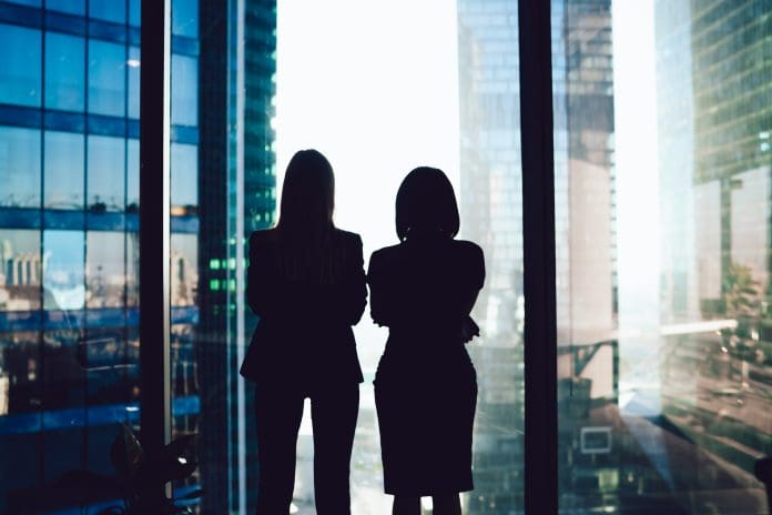Back view of female colleagues in formal wear standing near window looking at modern exterior of skyscrapers in business center, silhouette of women together planning future success of brainstorming buildingSMART International and Women in BIM join forces to advance digital innovation and inclusion